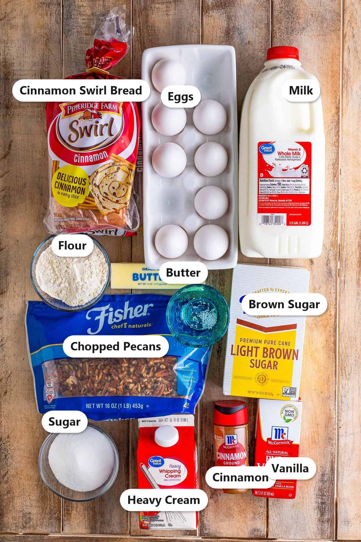 Labeled ingredients for overnight French toast casserole including cinnamon swirl bread, eggs, milk, heavy cream, sugar, brown sugar, flour, butter, pecans, cinnamon, and vanilla.