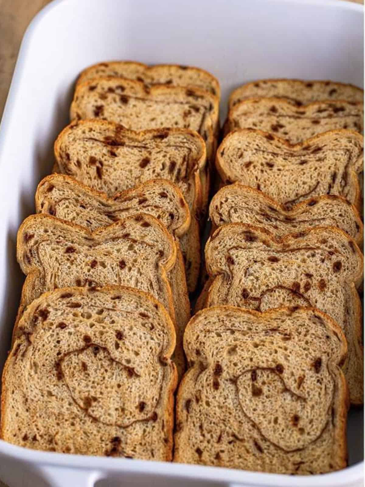 Cinnamon swirl bread slices layered in a greased baking dish.