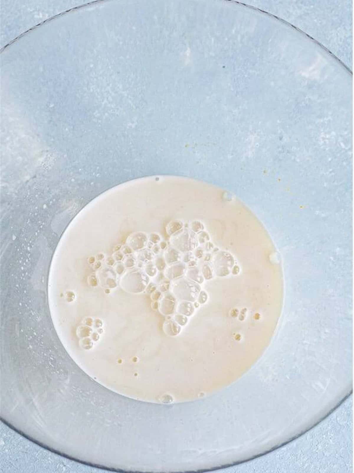 Warm milk and active dry yeast proofing in a glass bowl for air fryer cinnamon rolls.