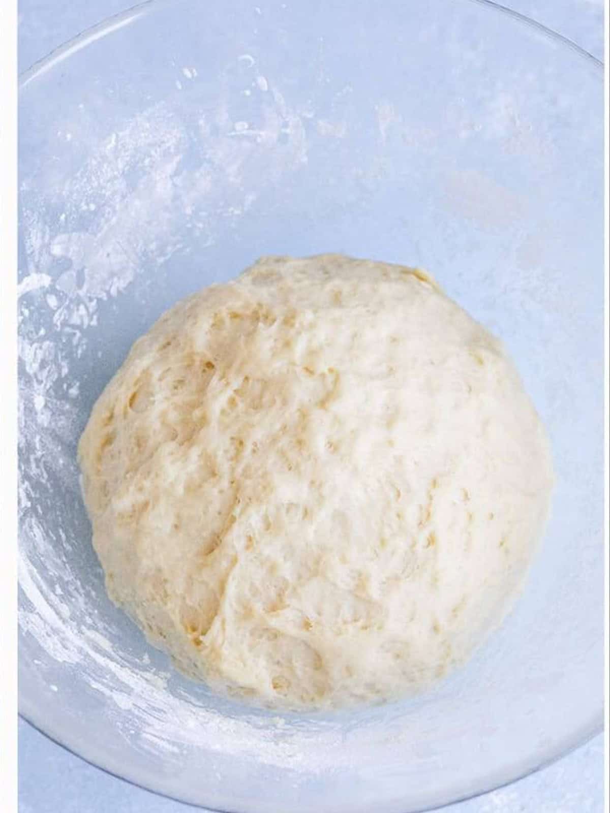A smooth ball of risen cinnamon roll dough in a glass bowl.