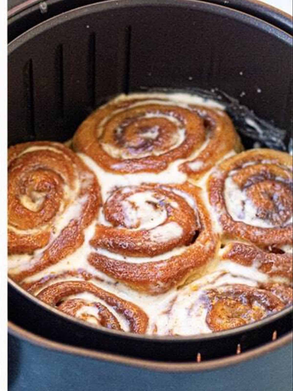 Cinnamon rolls baked golden in a parchment-lined air fryer basket.