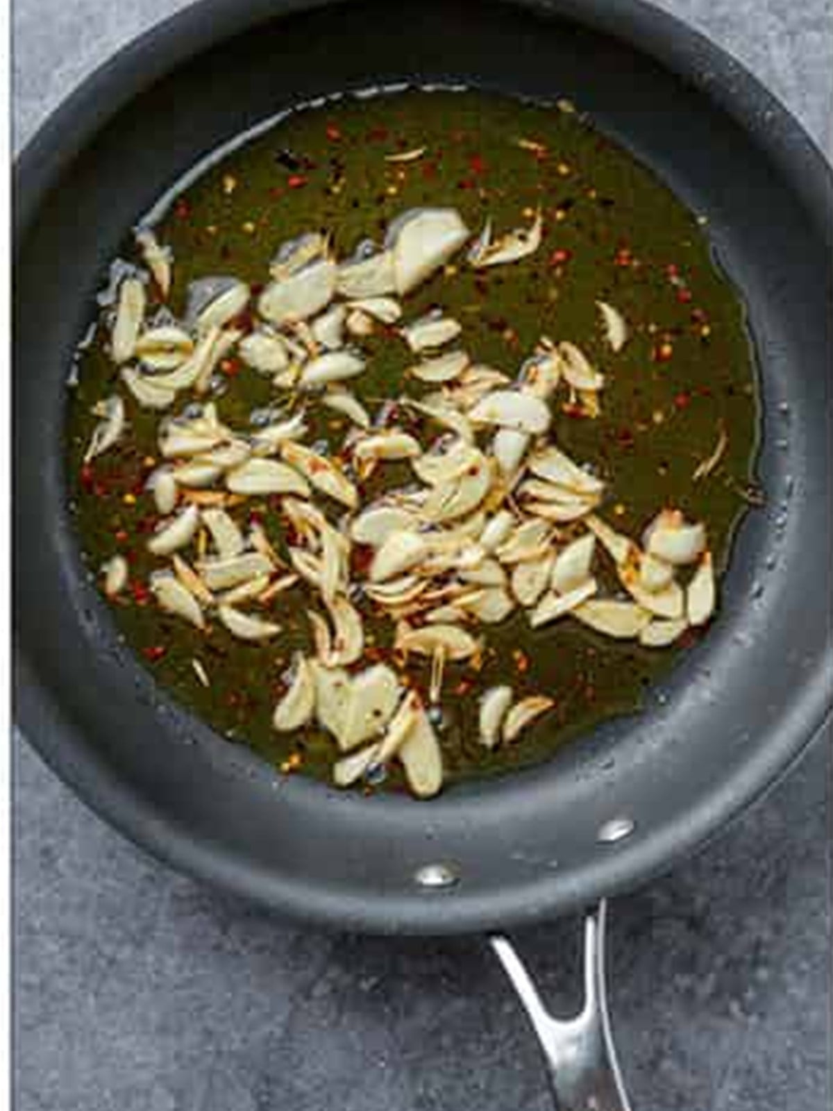 Sauteing sliced garlic and red pepper flakes in olive oil for Aglio e Olio.
