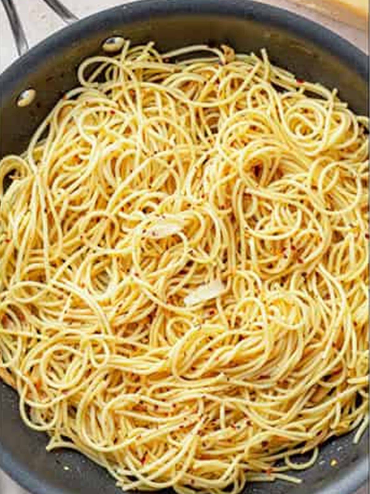 Tossing drained spaghetti into the garlic oil with pasta water for Aglio e Olio.