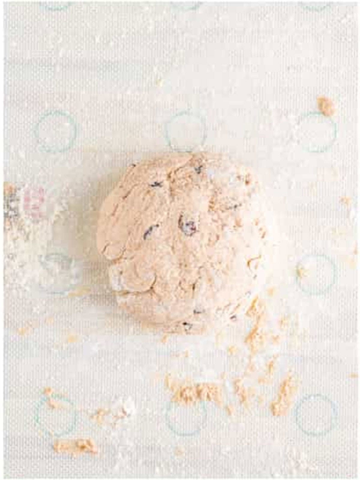 Cinnamon raisin bagel dough kneaded into a ball on a floured surface.