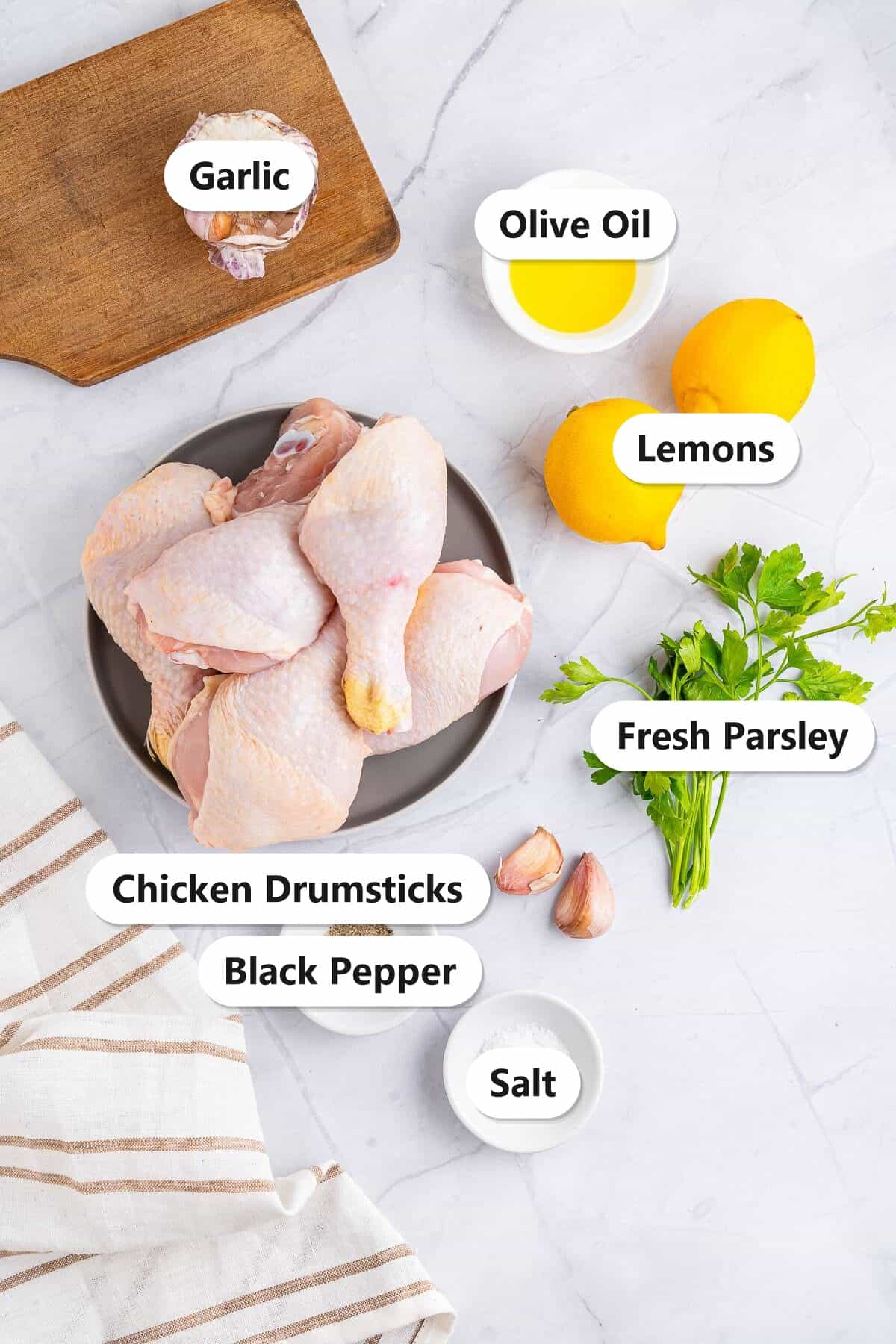 Labeled ingredients for air fryer chicken drumsticks including drumsticks, lemons, garlic, parsley, olive oil, salt, and pepper.