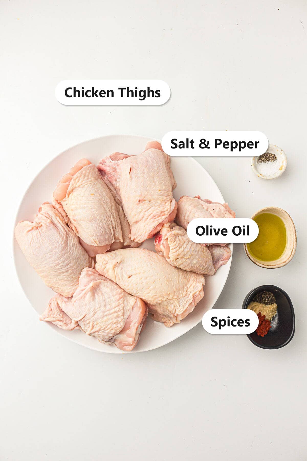 Labeled ingredients for air fryer chicken thighs including chicken thighs, olive oil, salt and pepper, and a blend of spices.