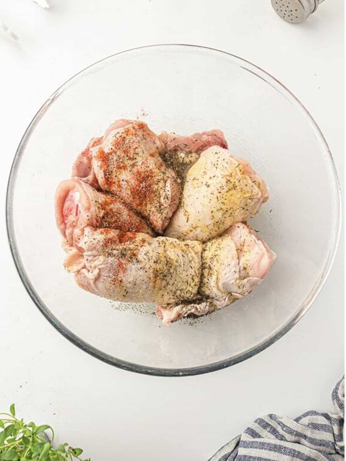 Raw chicken thighs in a bowl with the olive oil and spice mixture for air fryer chicken thighs.