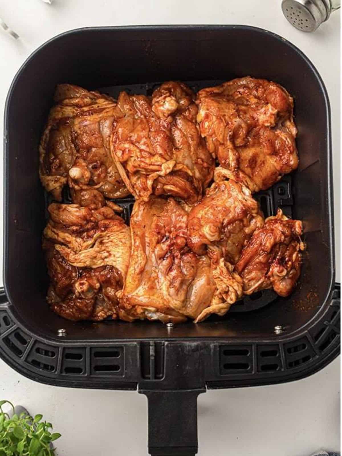 Seasoned chicken thighs arranged in an air fryer basket before cooking for air fryer chicken thighs.