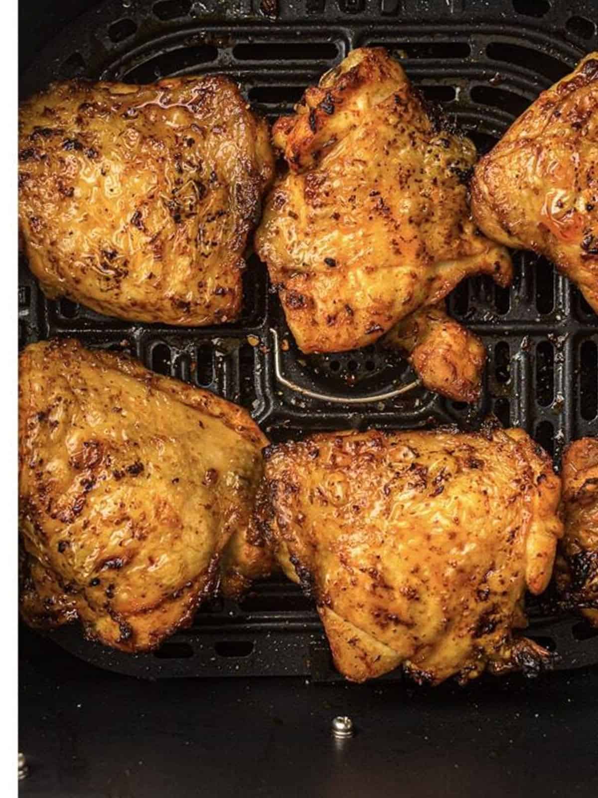 Golden crispy finished air fryer chicken thighs in the basket.