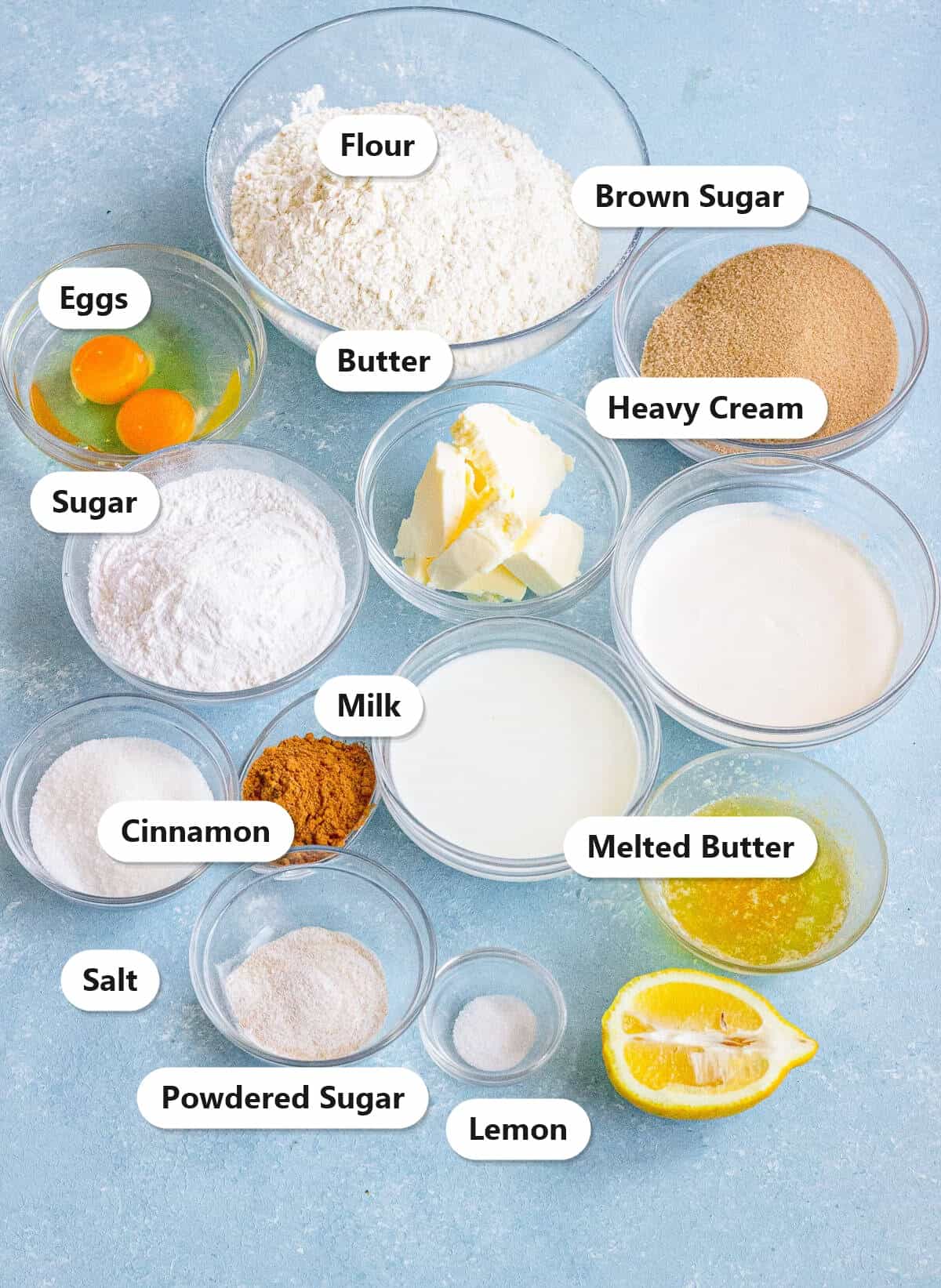 Labeled ingredients for air fryer cinnamon rolls including flour, brown sugar, eggs, butter, milk, cinnamon, and heavy cream.