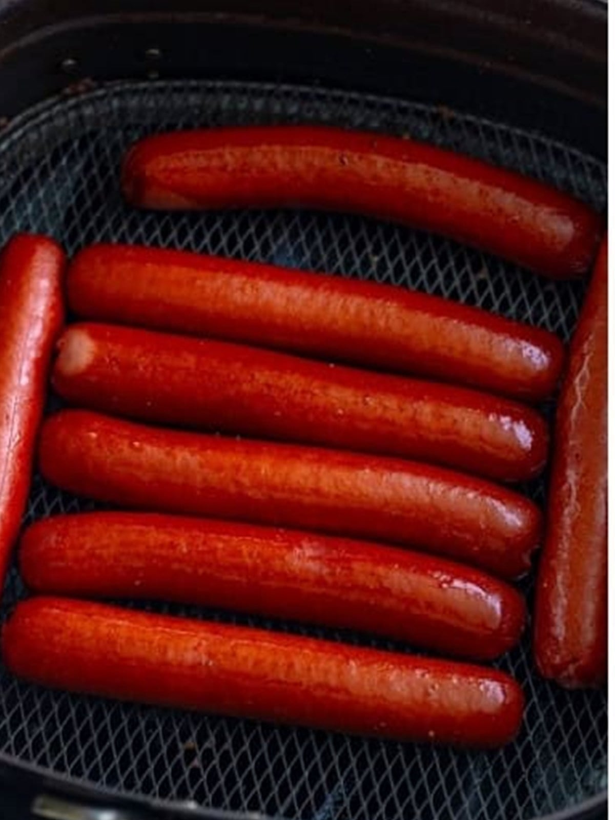 Hot dogs cooking in a single layer in the air fryer basket.