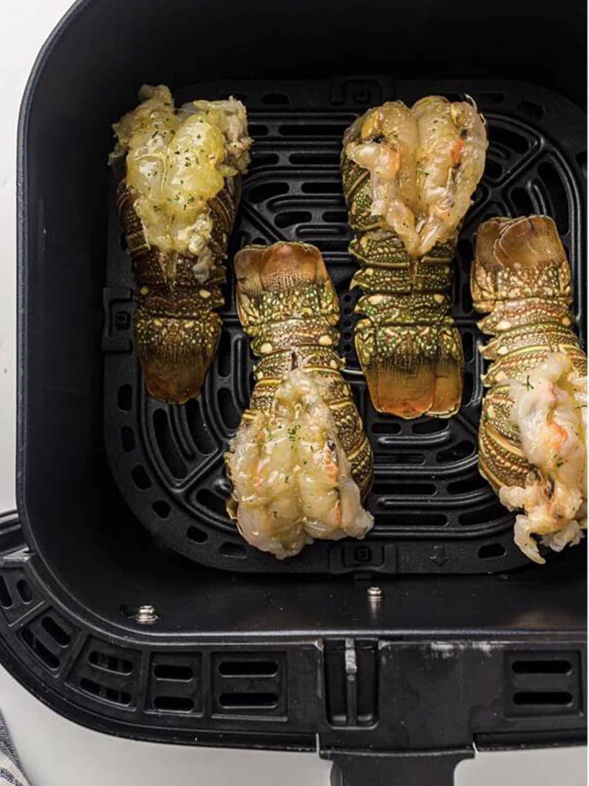 Lobster tails placed shell side down in an air fryer basket.