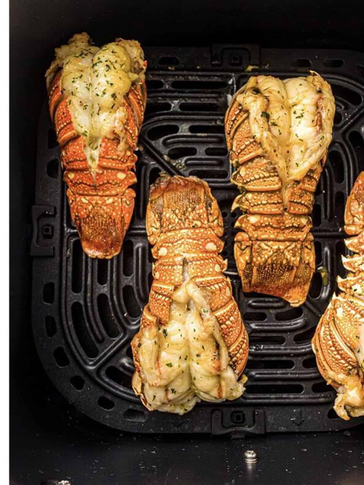 Cooked lobster tails with opaque meat in an air fryer basket.