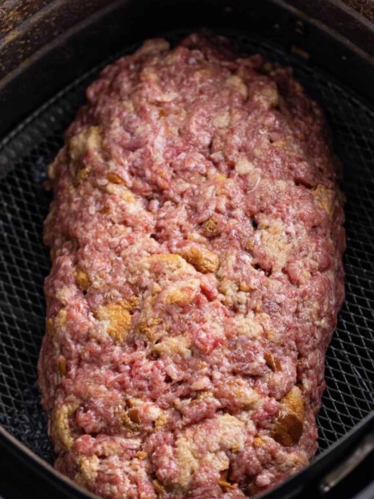 Raw meatloaf shaped at an angle in the air fryer basket.