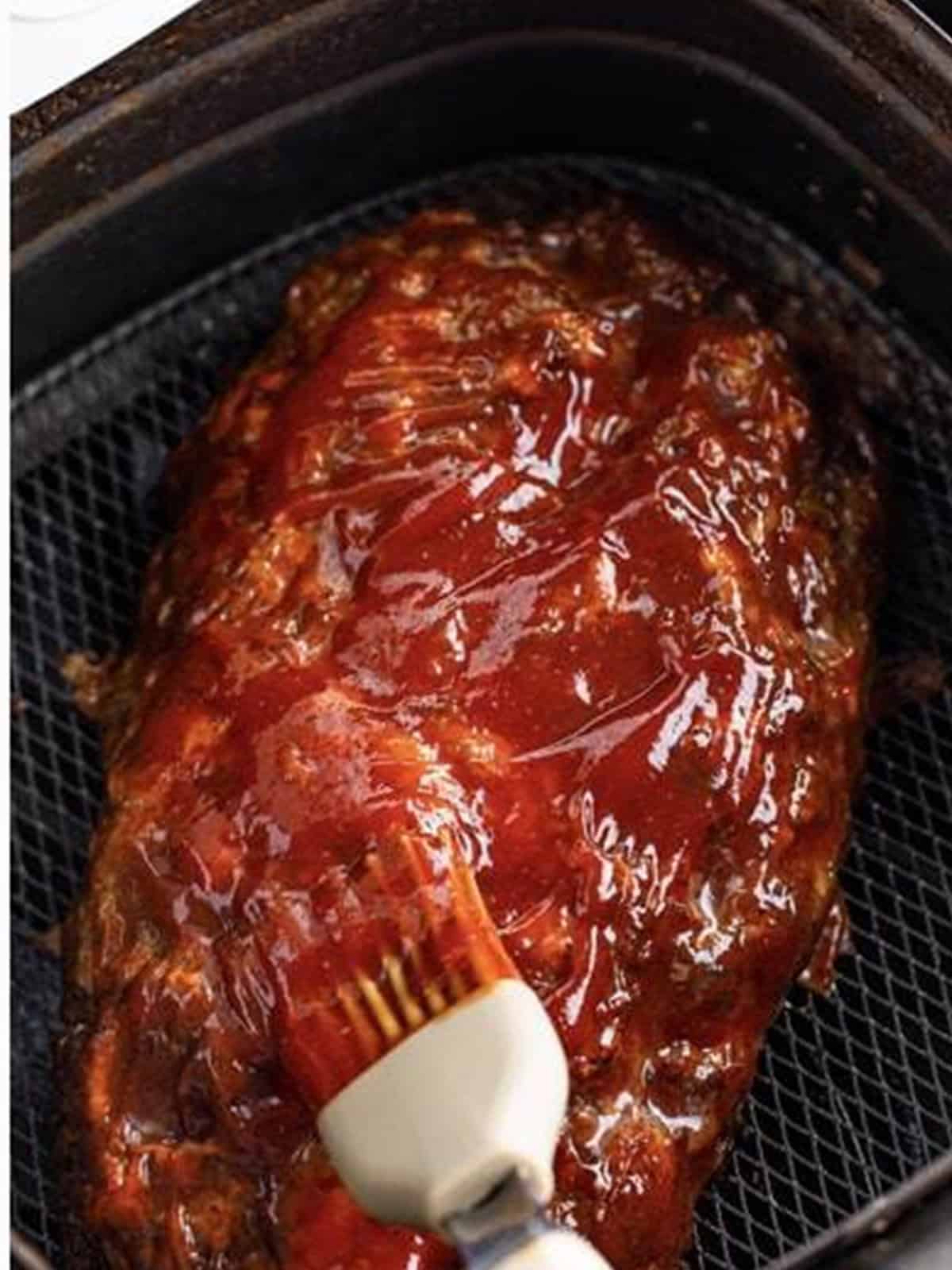 Brushing the glaze over the air fryer meatloaf in the basket.