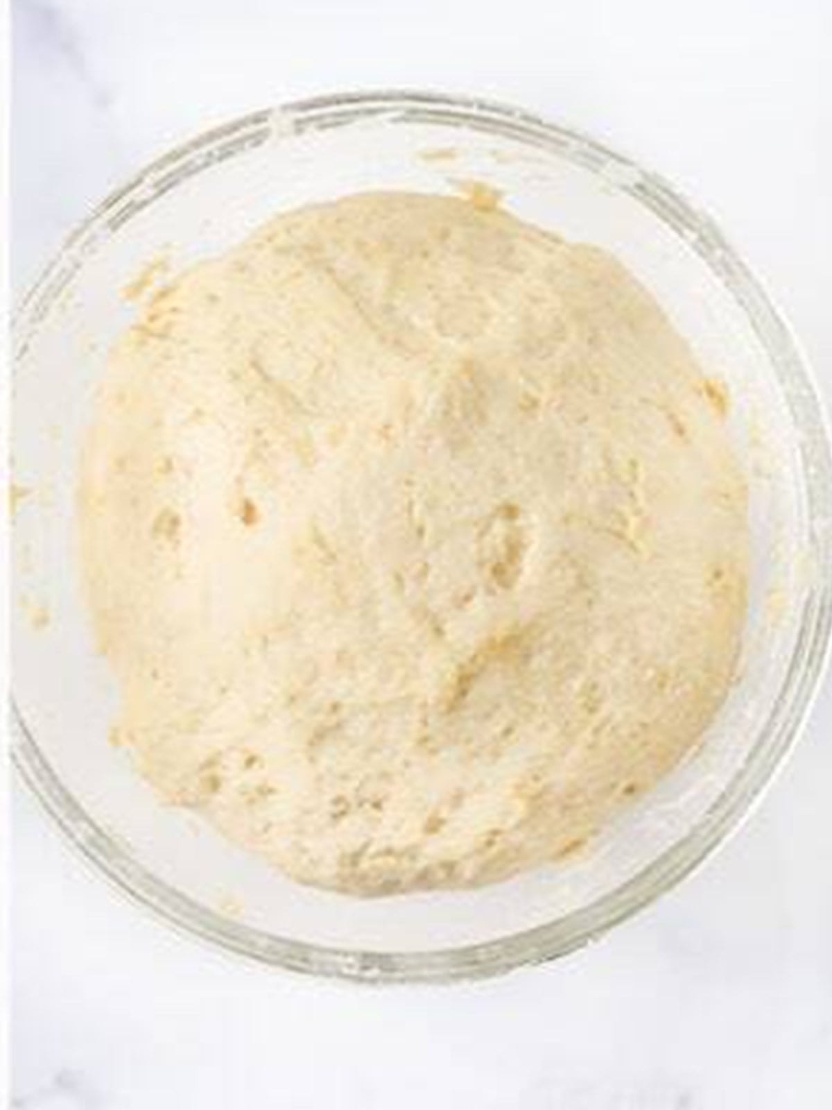Risen soft naan dough doubled in size in a glass bowl.