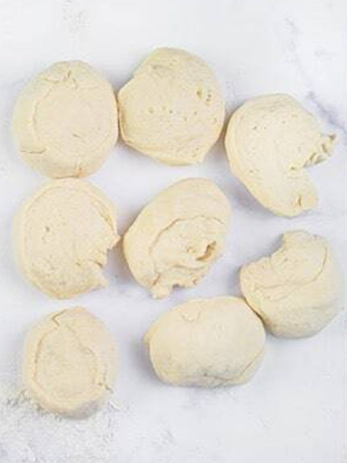 Eight divided naan dough balls on a floured surface.