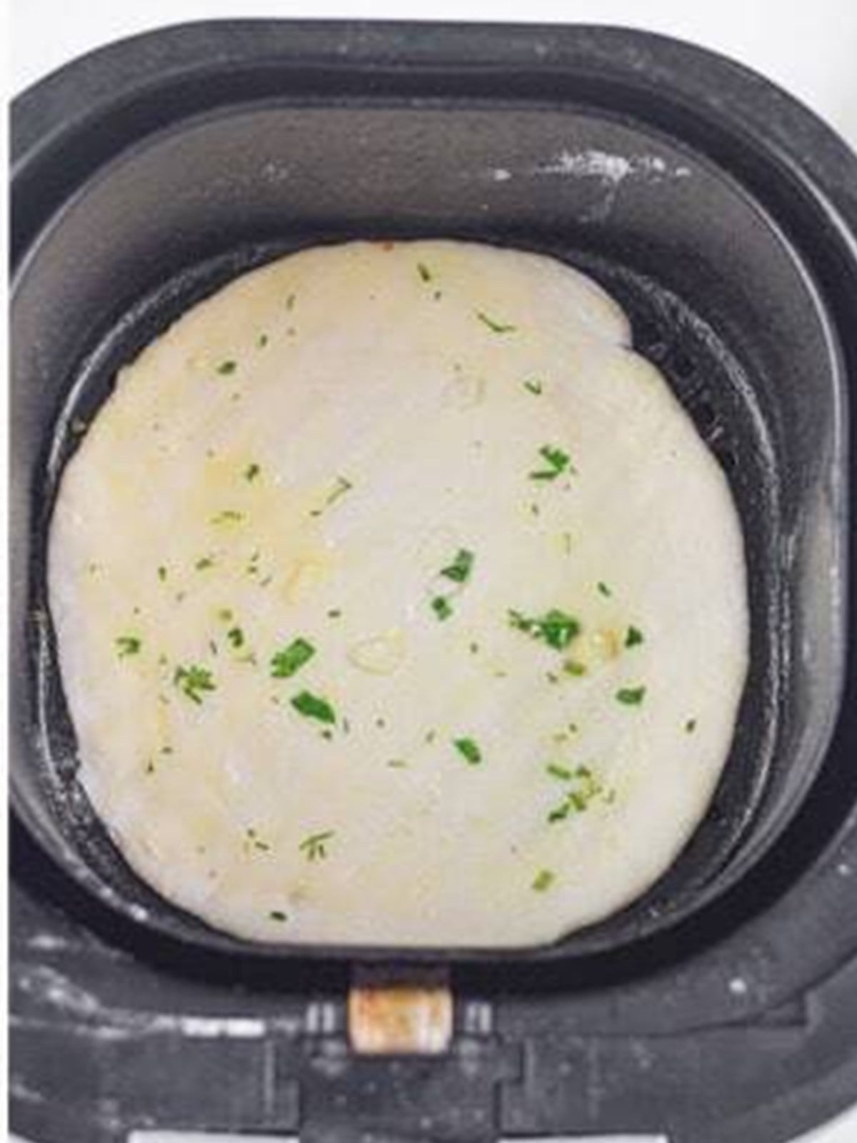Raw garlic naan brushed with butter cooking in an air fryer basket.