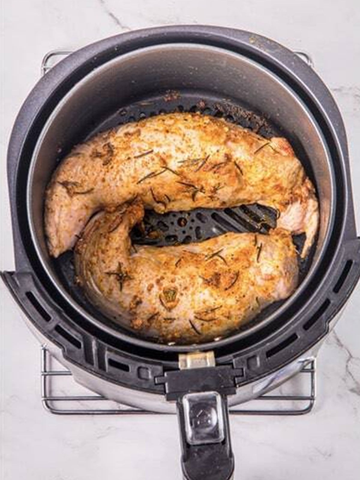 Seasoned pork tenderloins arranged in the air fryer basket.