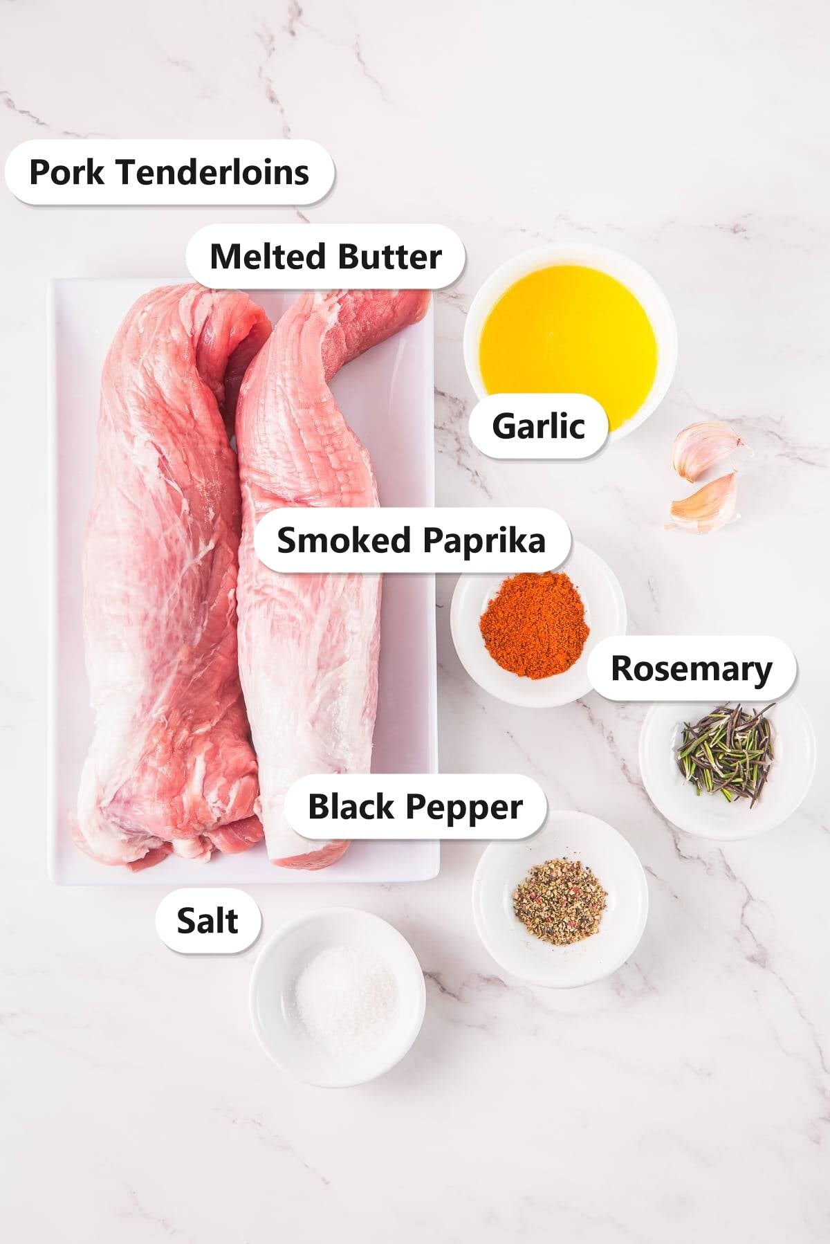 Air Fryer Pork Tenderloin ingredients including pork tenderloins, melted butter, garlic, smoked paprika, rosemary, salt, and pepper labeled on a marble counter.