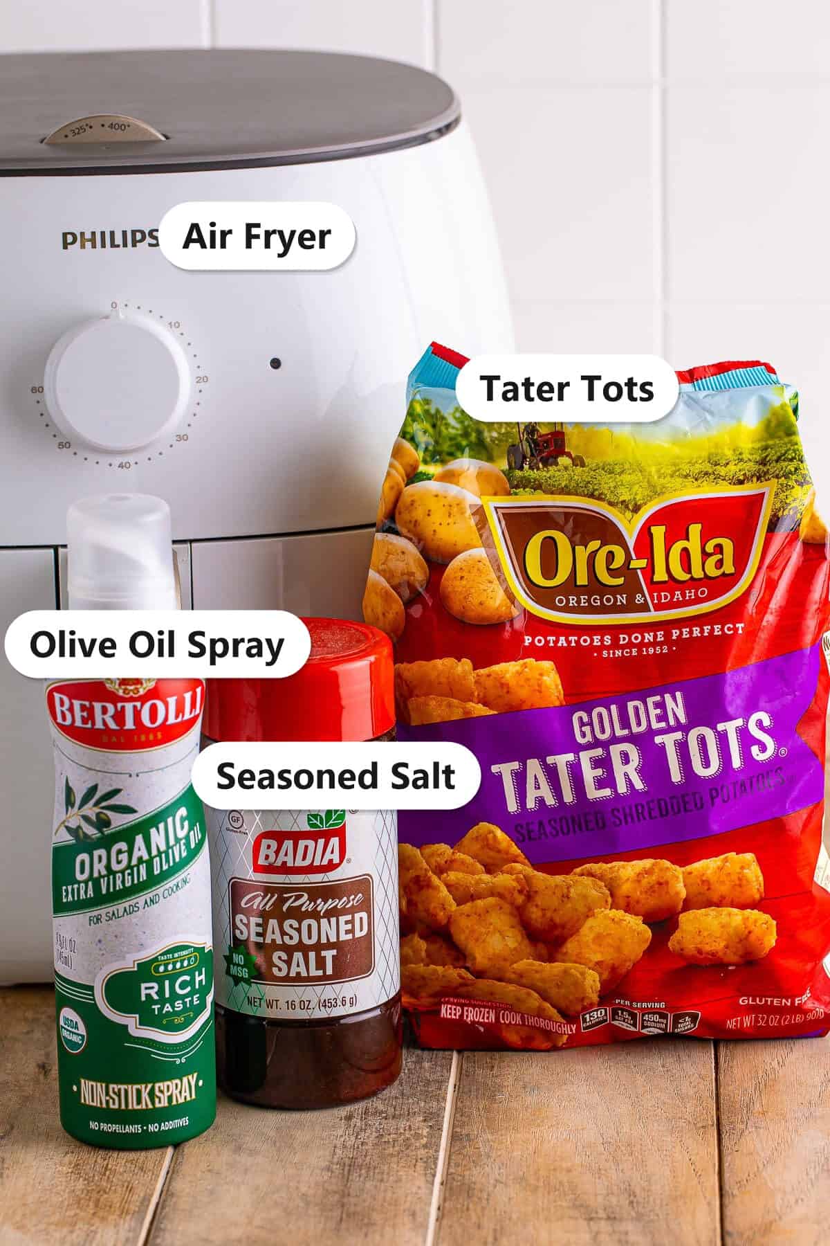 Labeled ingredients for air fryer tater tots including frozen Ore-Ida tater tots, olive oil spray, and seasoned salt with an air fryer.