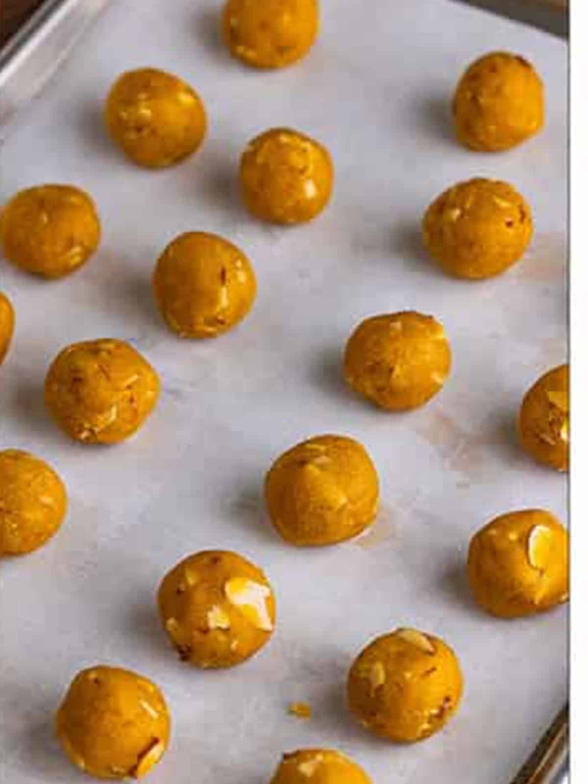 Rolled almond cookie dough balls on a parchment-lined baking sheet.