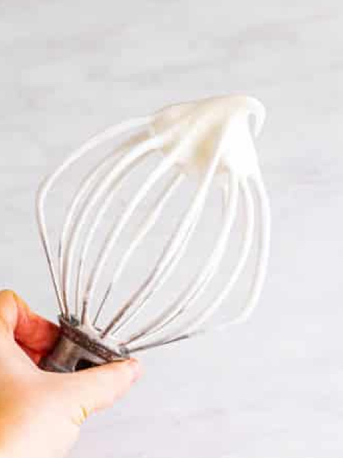 A whisk lifting glossy soft peaks of whipped egg whites for angel food cake.