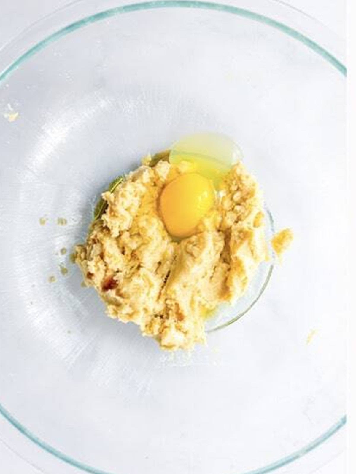 Creamed butter and sugars with an egg added in a glass bowl.