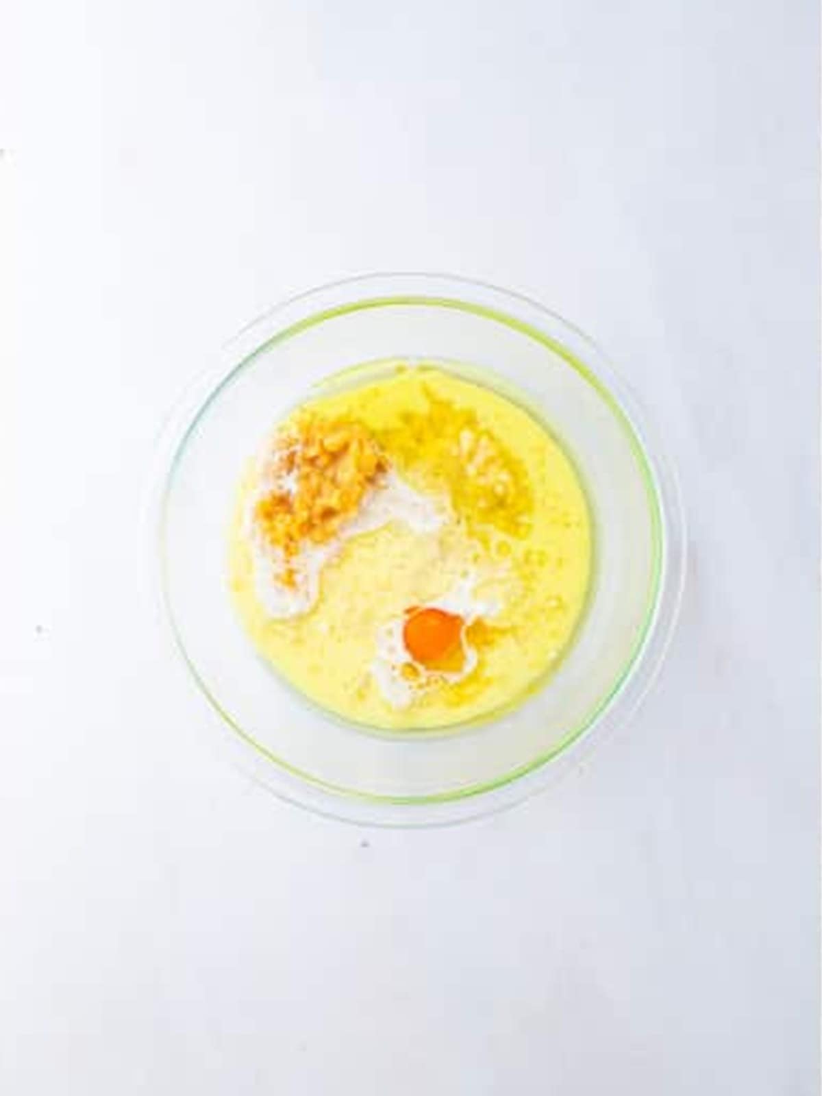 Egg, milk, oil, mashed bananas, and grated apple added to a separate bowl for apple banana muffins.