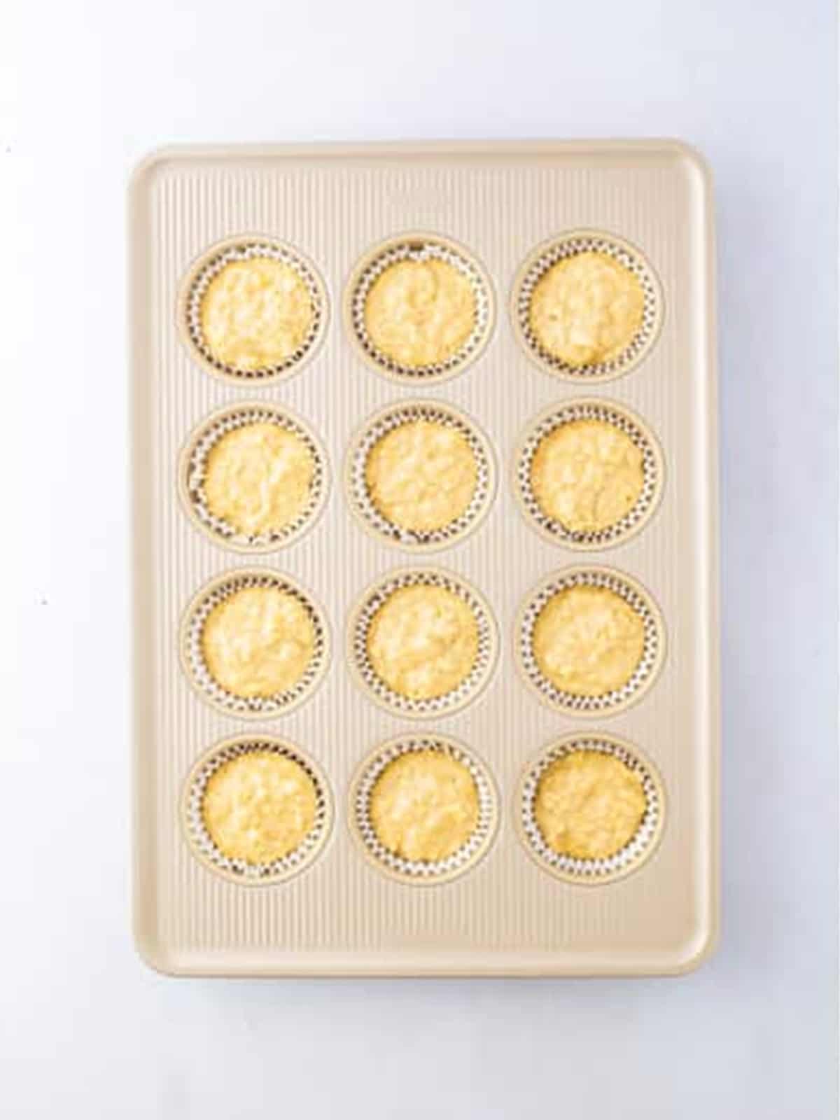 Muffin batter divided into a lined muffin tin and sprinkled with sugar.