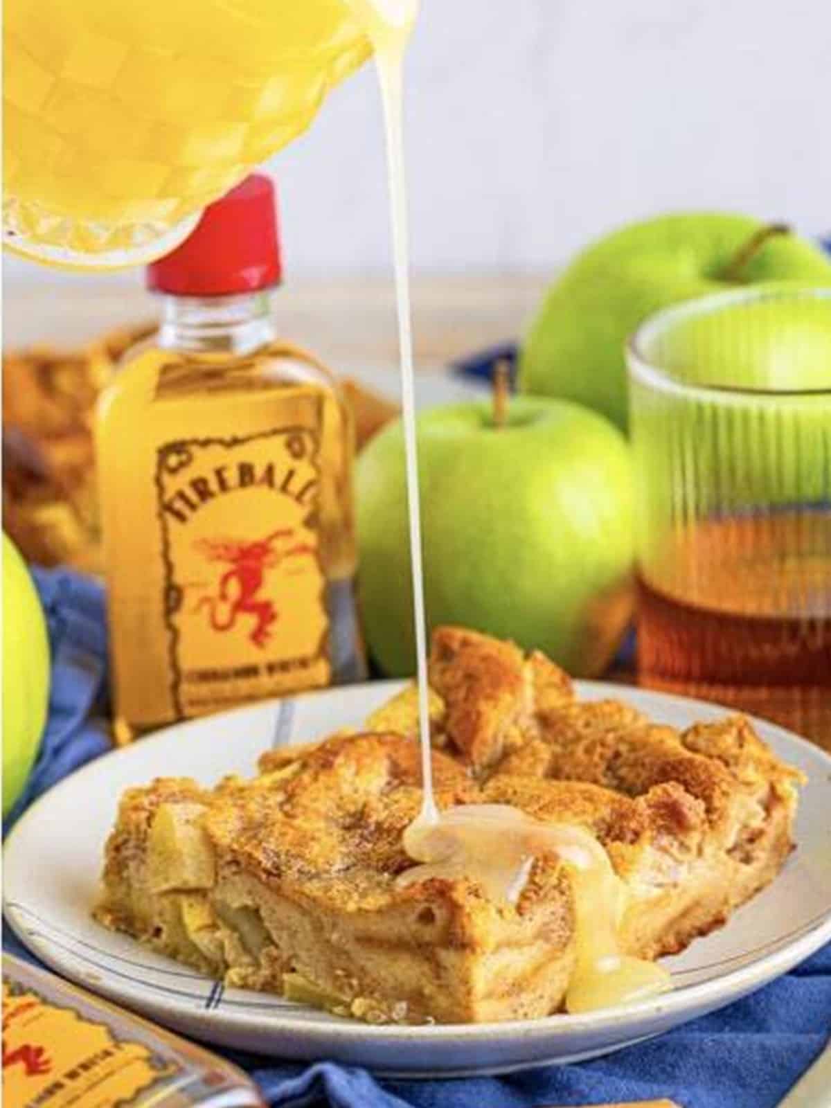 Warm Fireball caramel sauce being drizzled over a plated piece of apple bread pudding.