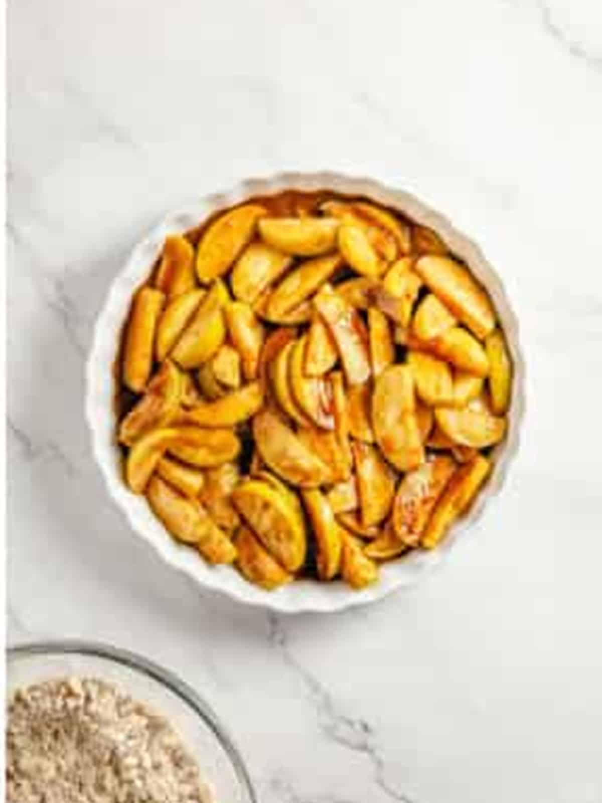 Cooked cinnamon apples spread in a round baking dish for apple crumble.