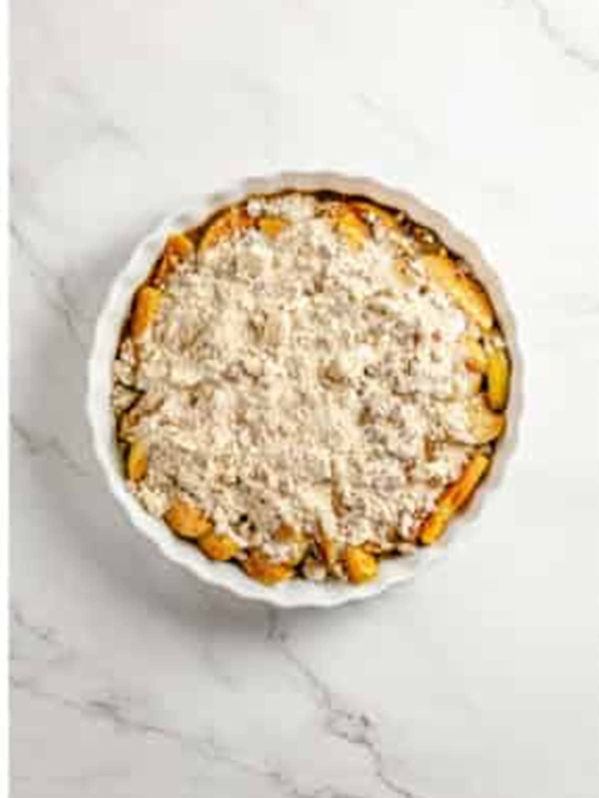 Crumble topping sprinkled over the cinnamon apples in a baking dish.