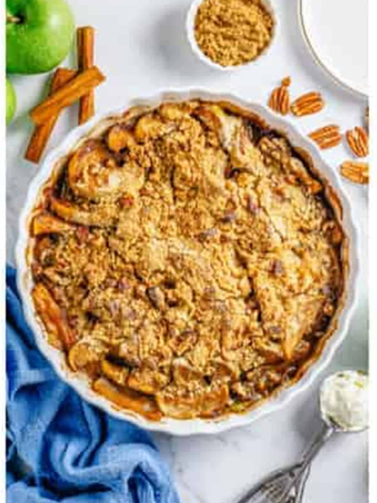A golden baked apple crumble bubbling in a round dish topped with pecans.