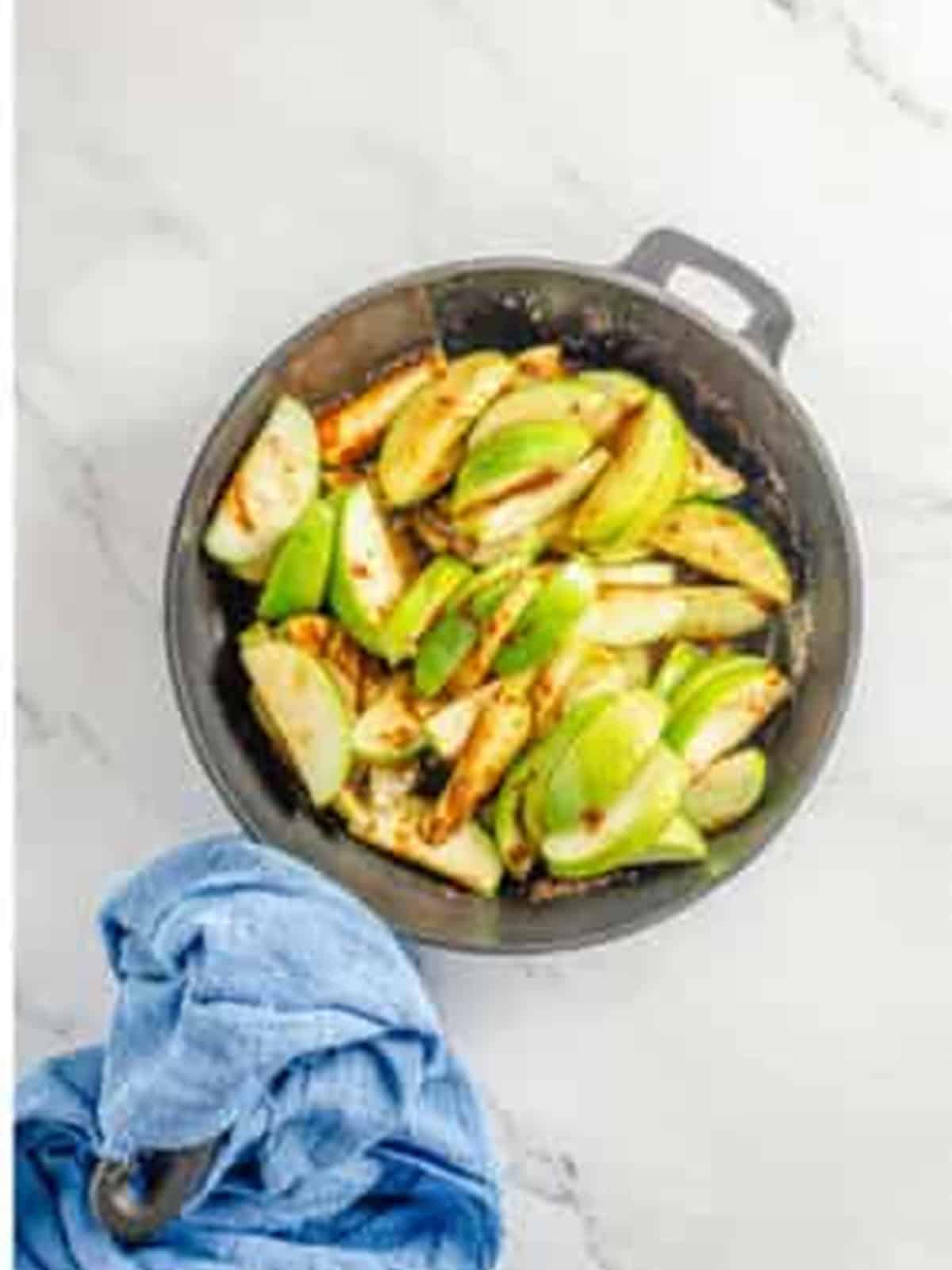 Apple slices cooking in a skillet with melted butter, brown sugar, and cinnamon.