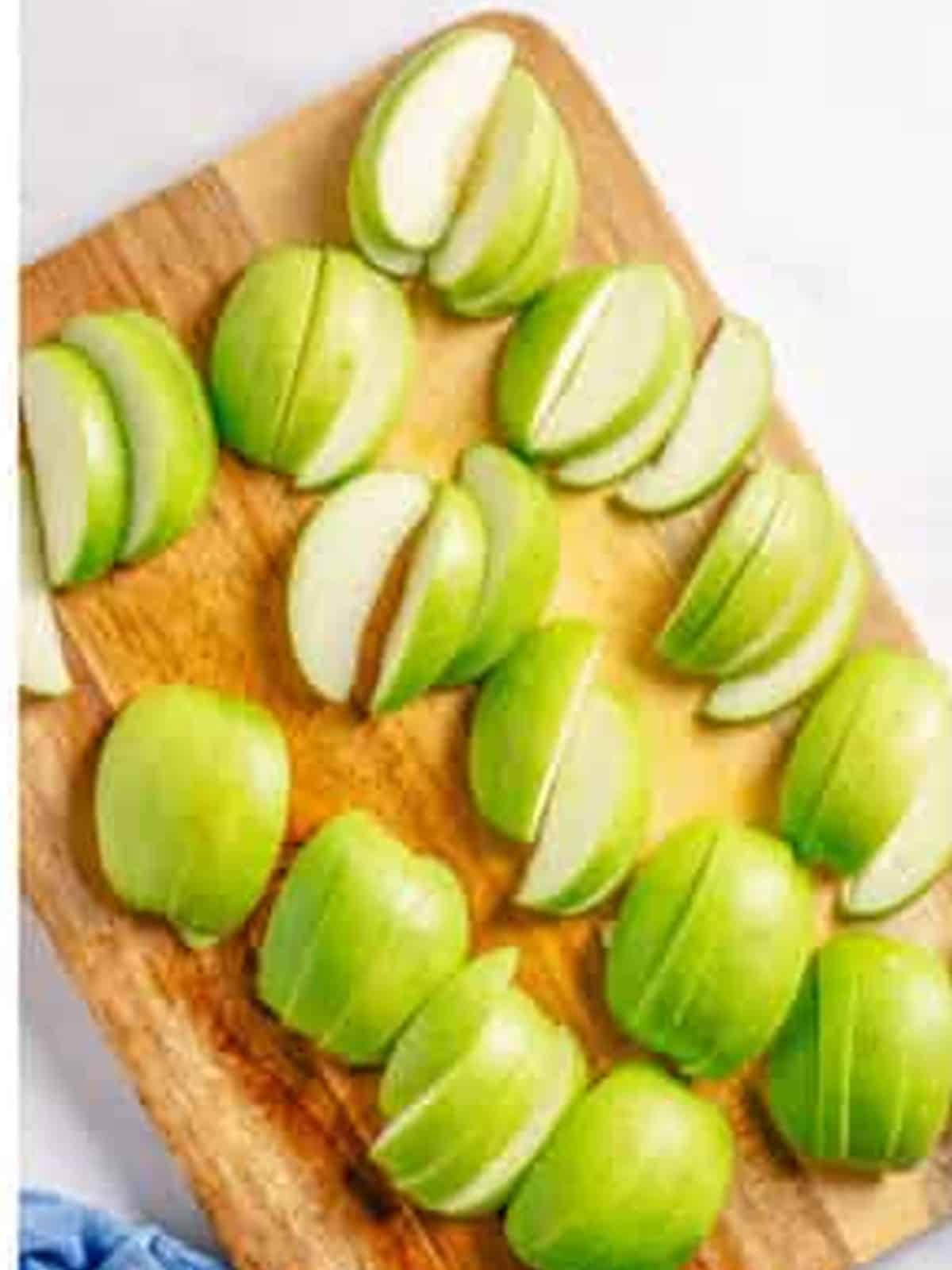 Sliced green granny smith apples on a wooden cutting board for apple crumble.