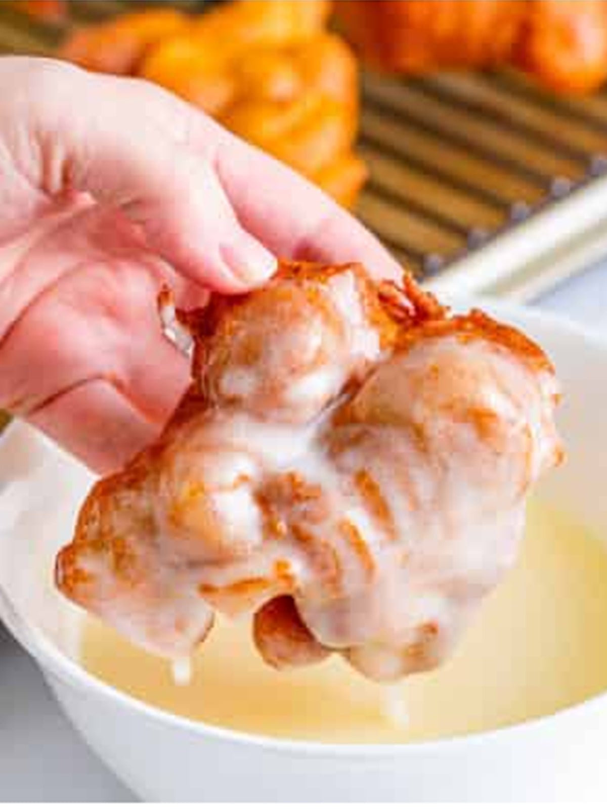 A fried apple fritter being dipped into sweet glaze.