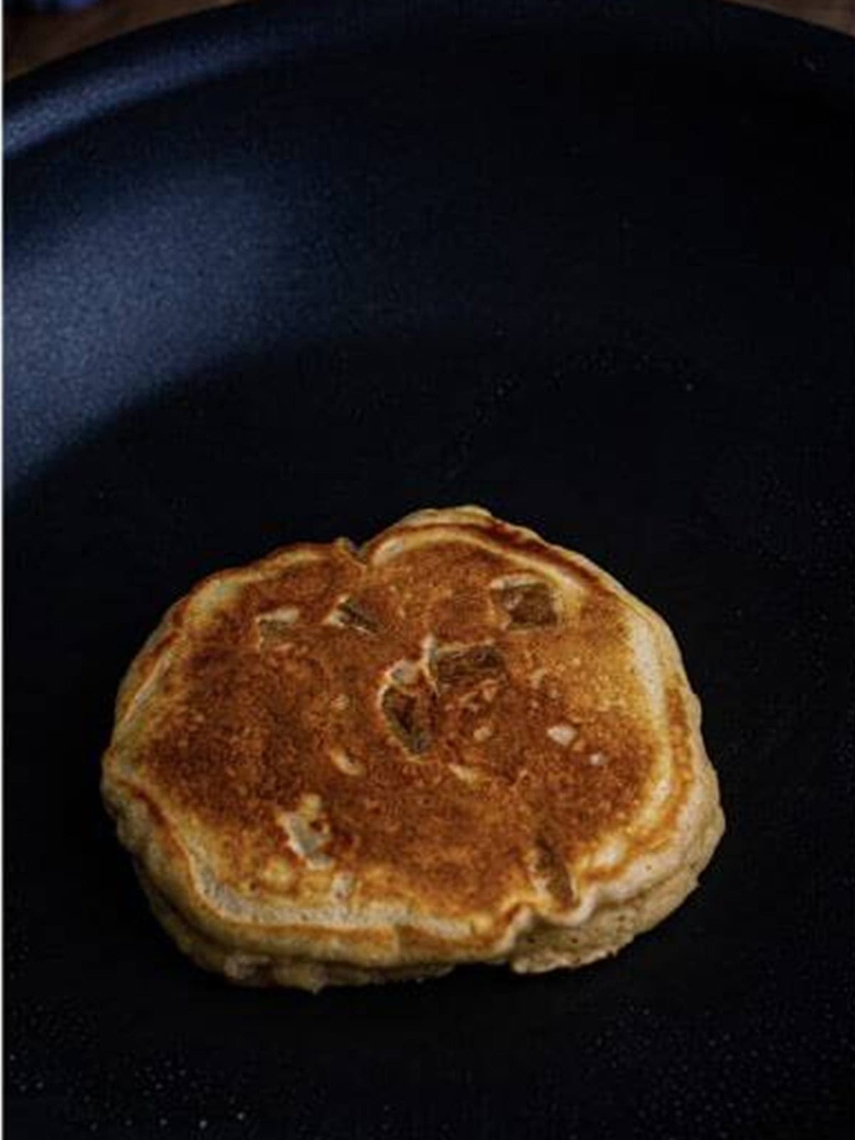 A golden apple pancake cooking in a nonstick skillet.