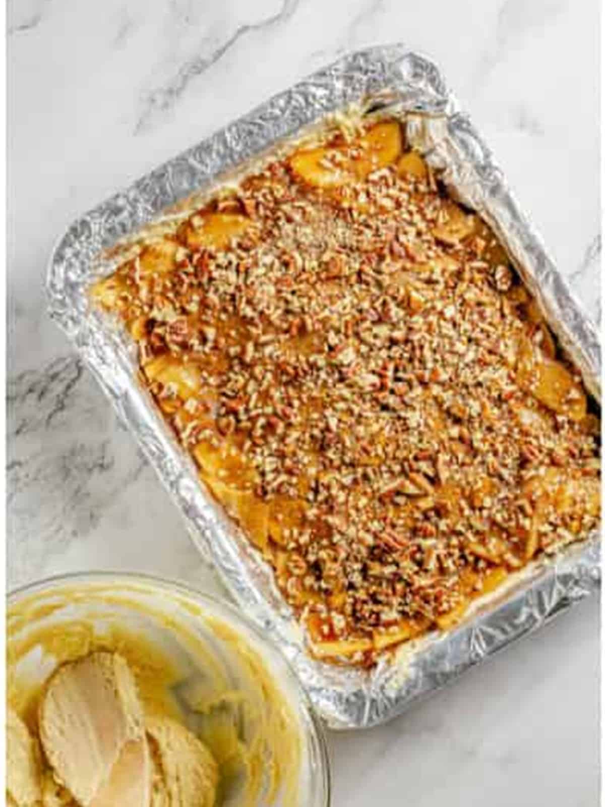 Spreading apple pie filling and pecans over the batter base in a pan.