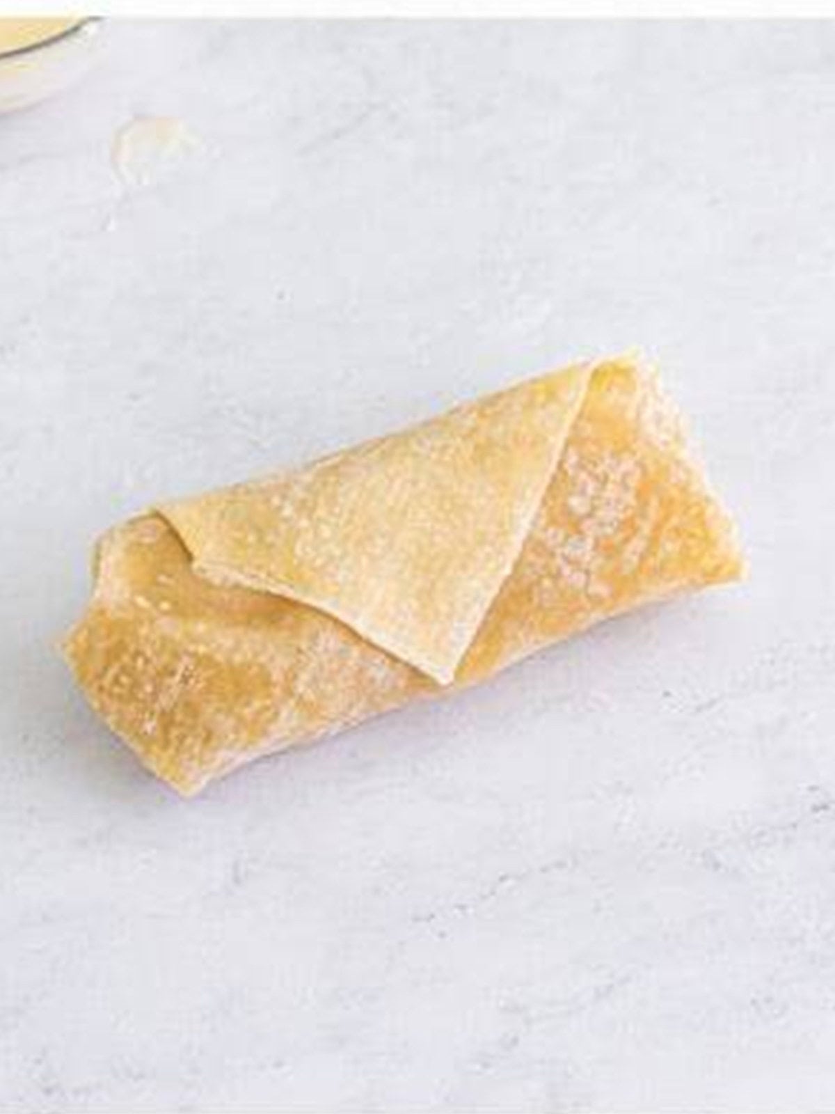 A rolled and sealed apple pie egg roll on a work surface.