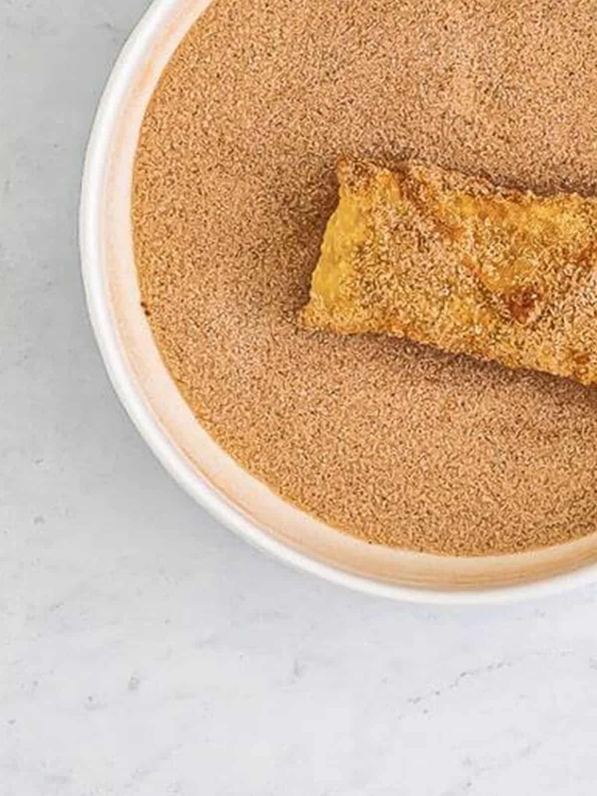 Rolling a fried apple pie egg roll in cinnamon sugar to coat it.