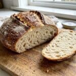 A rustic round artisan bread loaf with a golden crust, sliced to show the soft airy crumb.