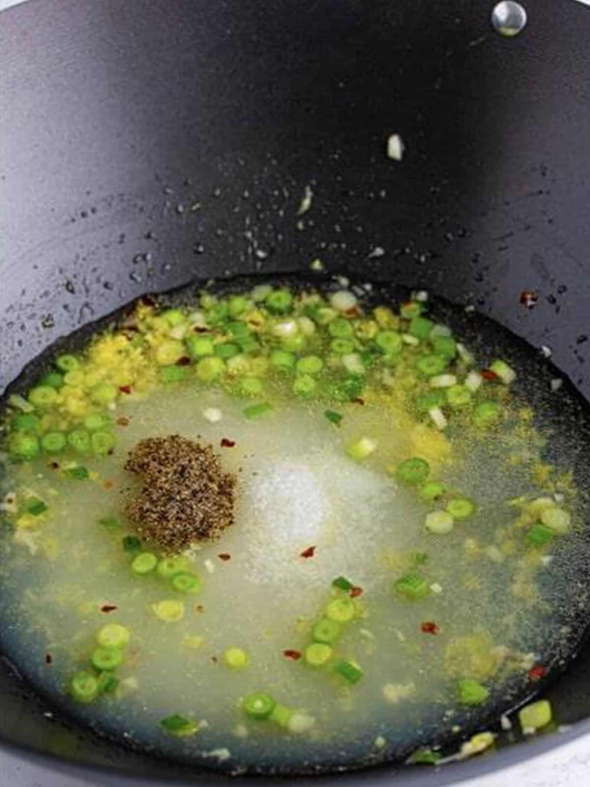 Adding water, sugar, lemon juice, salt, and pepper to the wok.