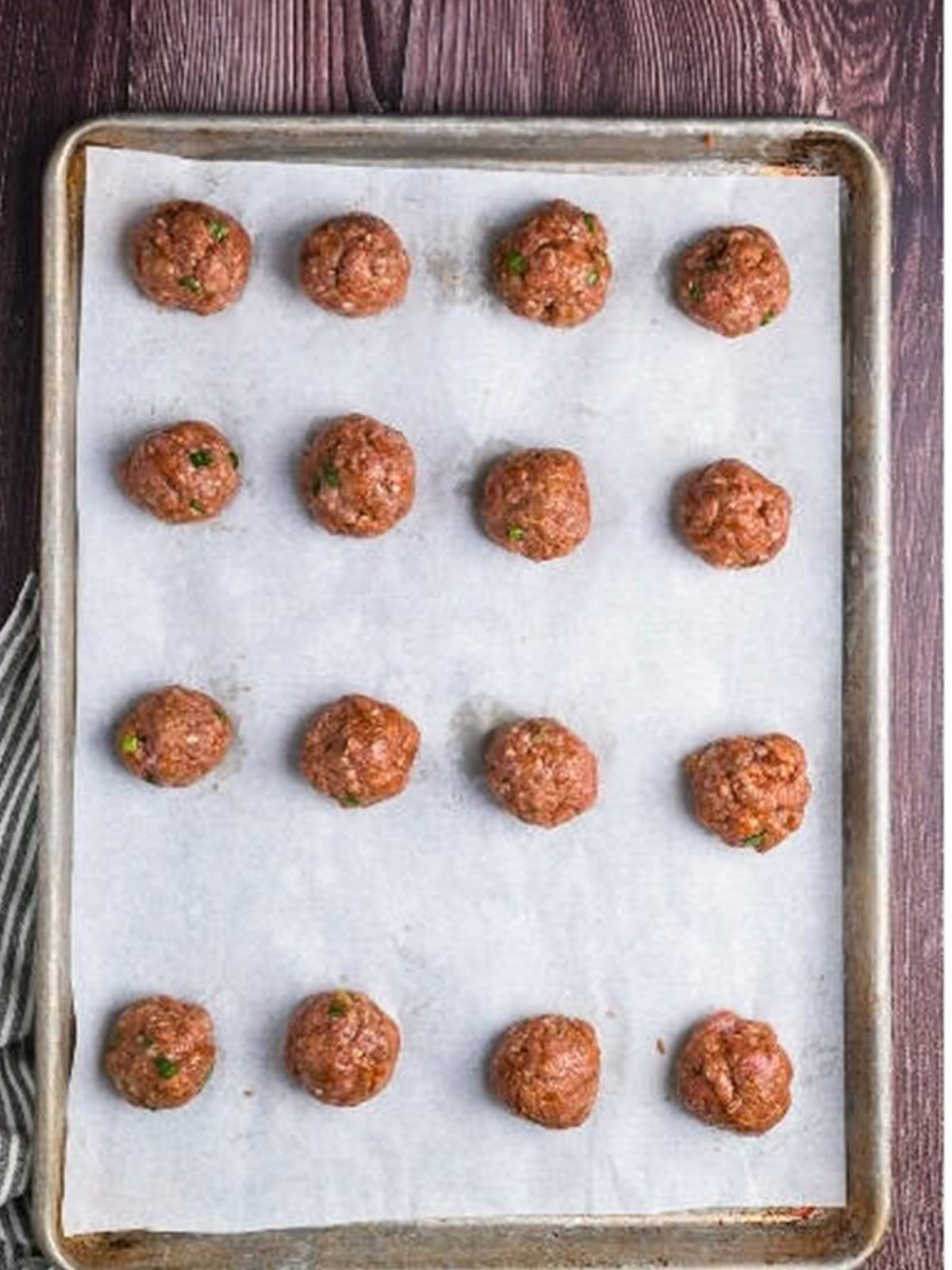 Raw Asian meatballs formed and spaced on a parchment lined baking sheet.