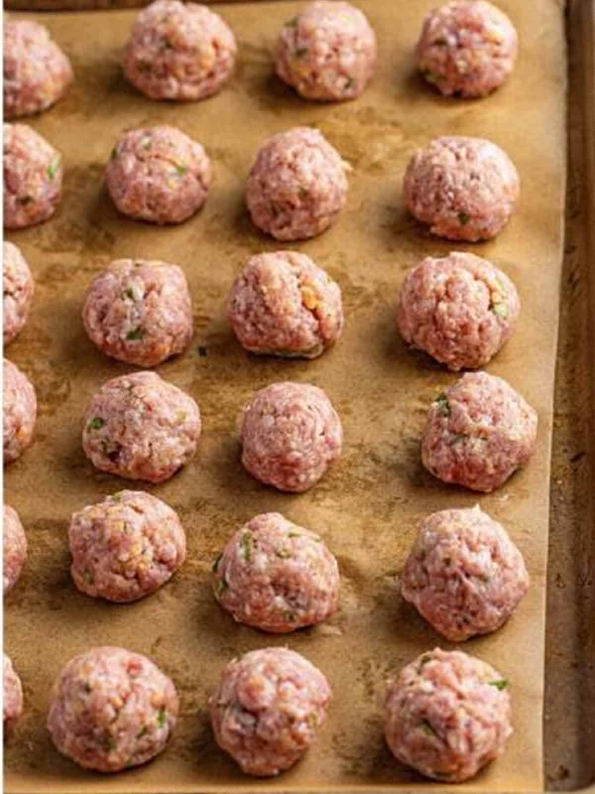 Raw Asian pork meatballs rolled on a parchment lined sheet tray.