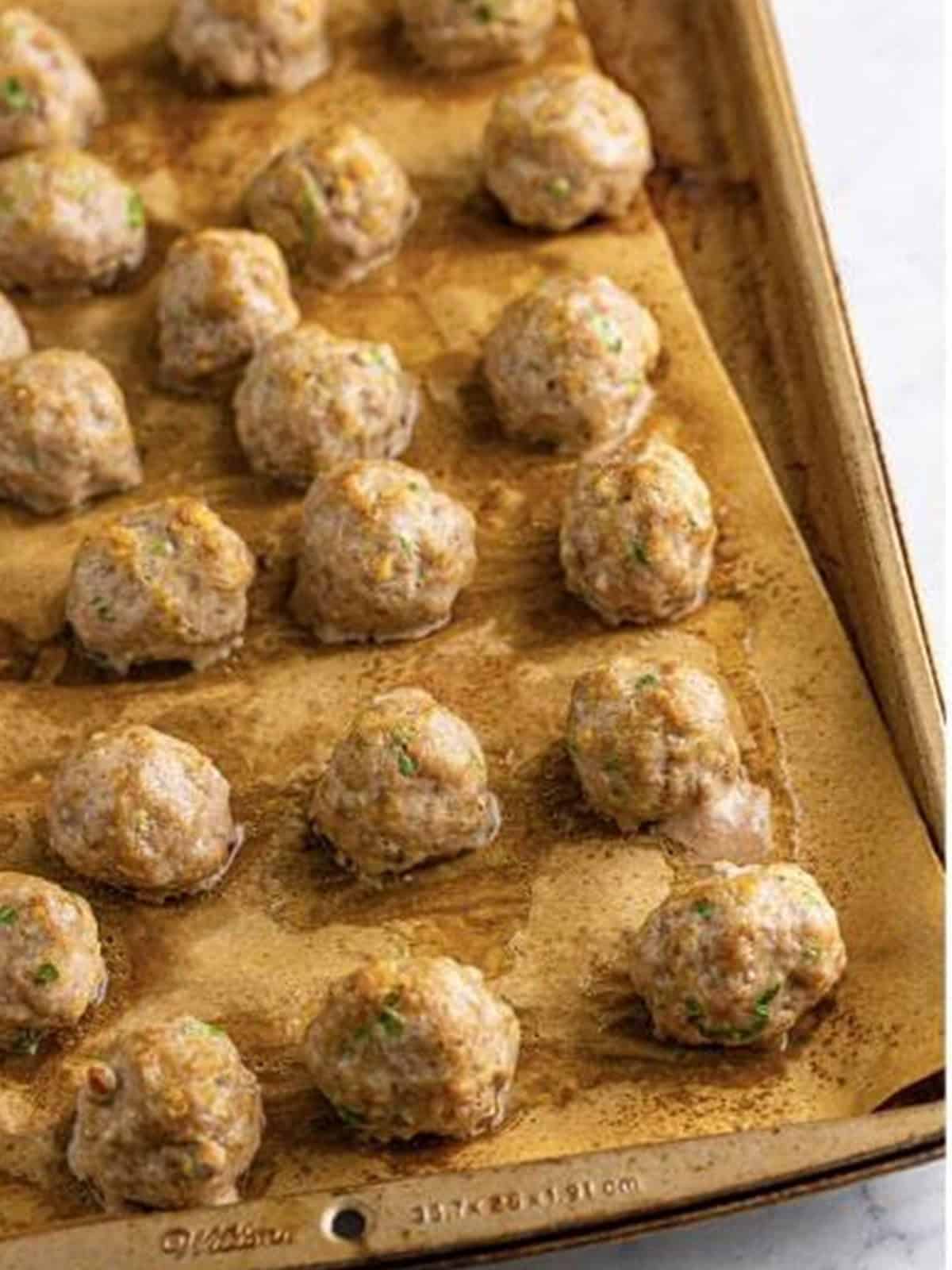 Baked Asian pork meatballs lightly golden on a sheet tray.
