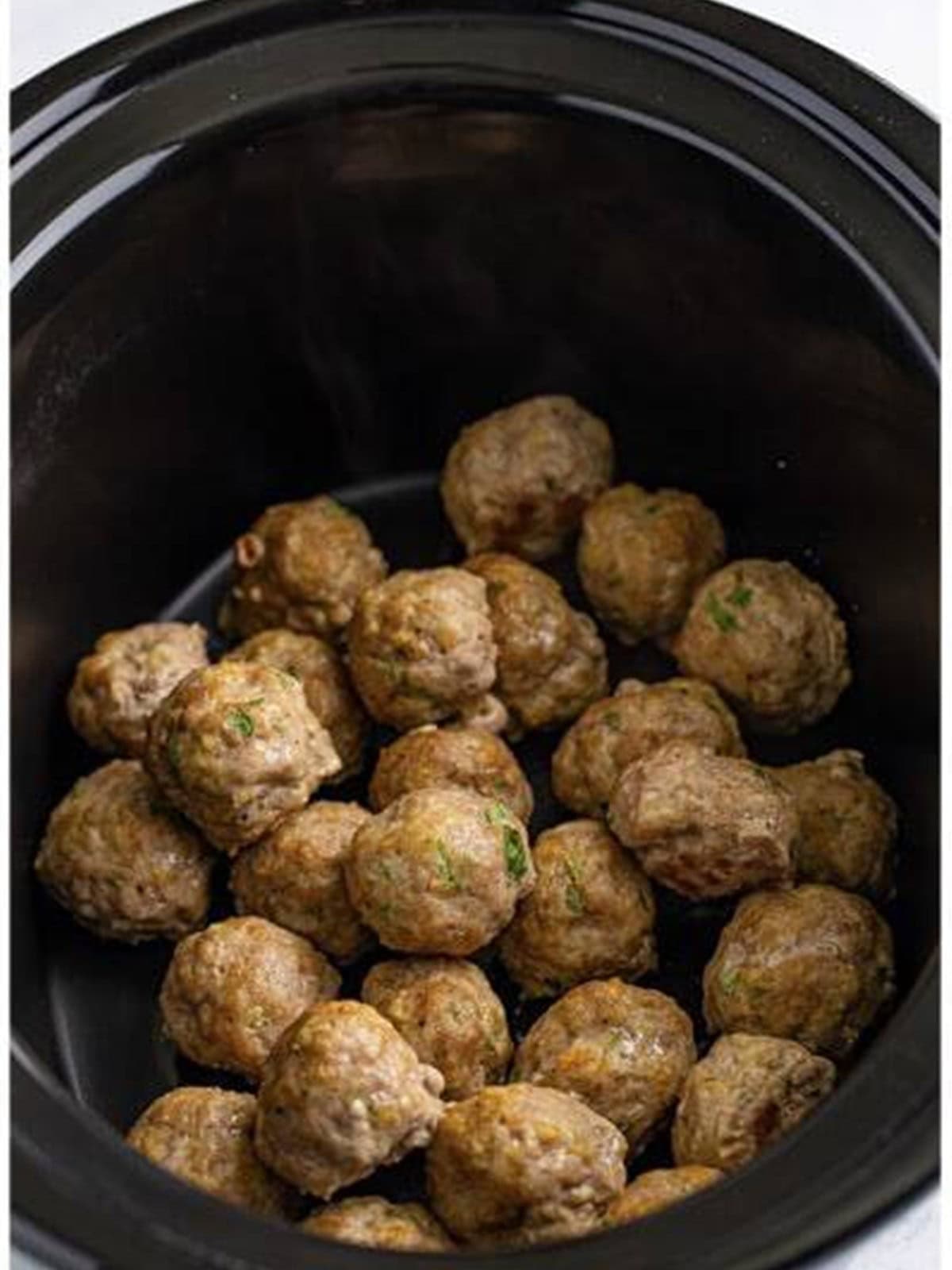Baked pork meatballs added to a slow cooker.