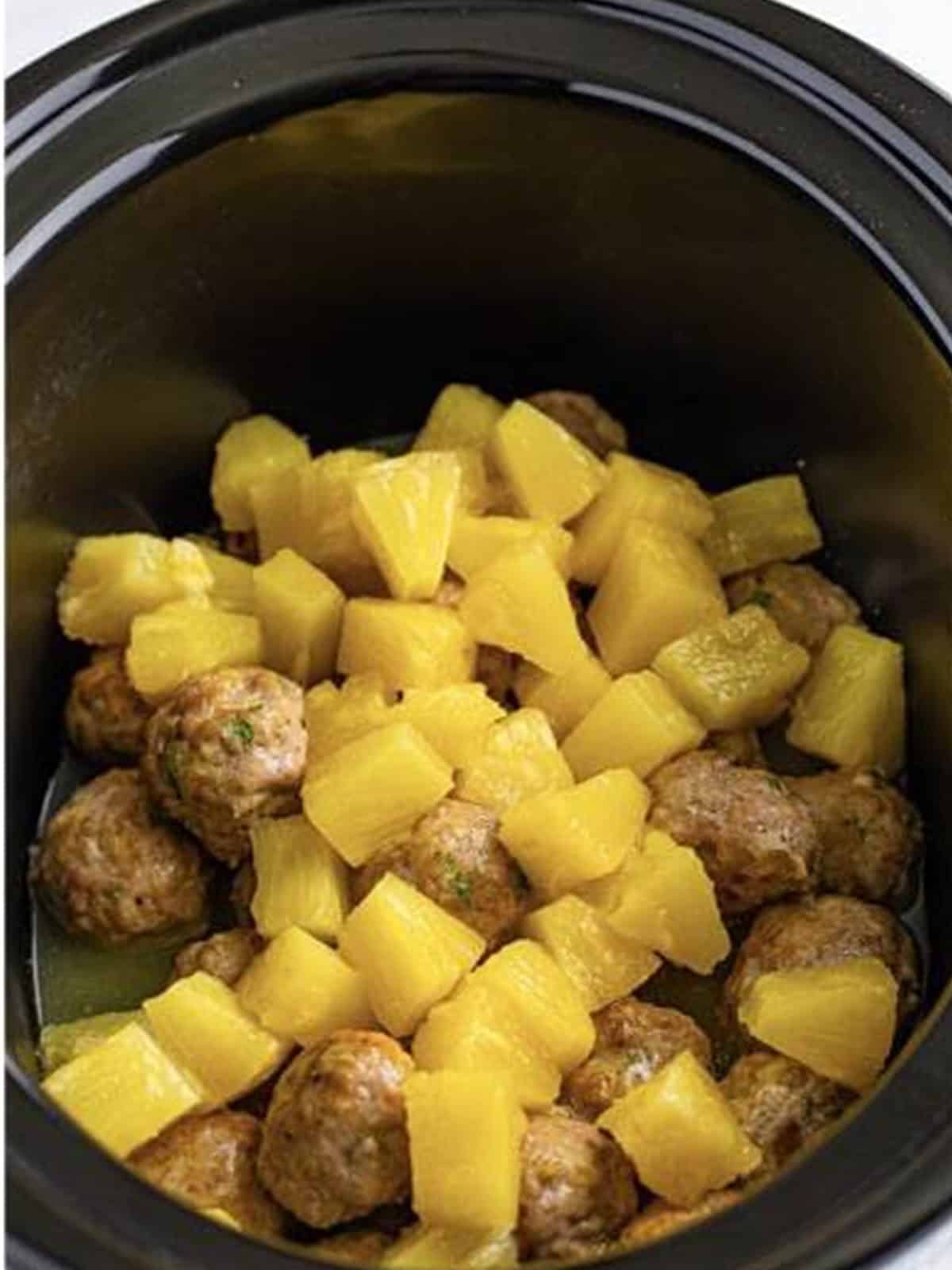 Pineapple chunks added to the meatballs in the slow cooker.