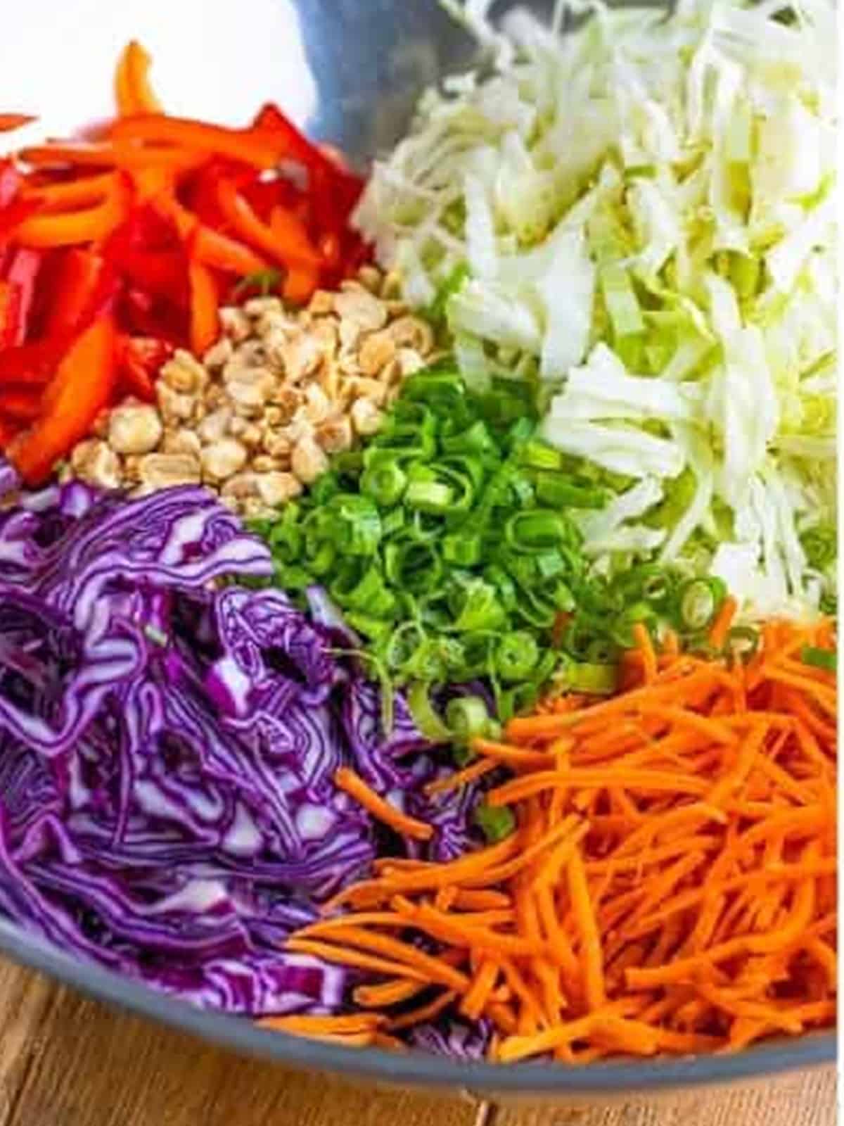 Shredded cabbage, carrots, bell pepper, scallions, and peanuts in a bowl.