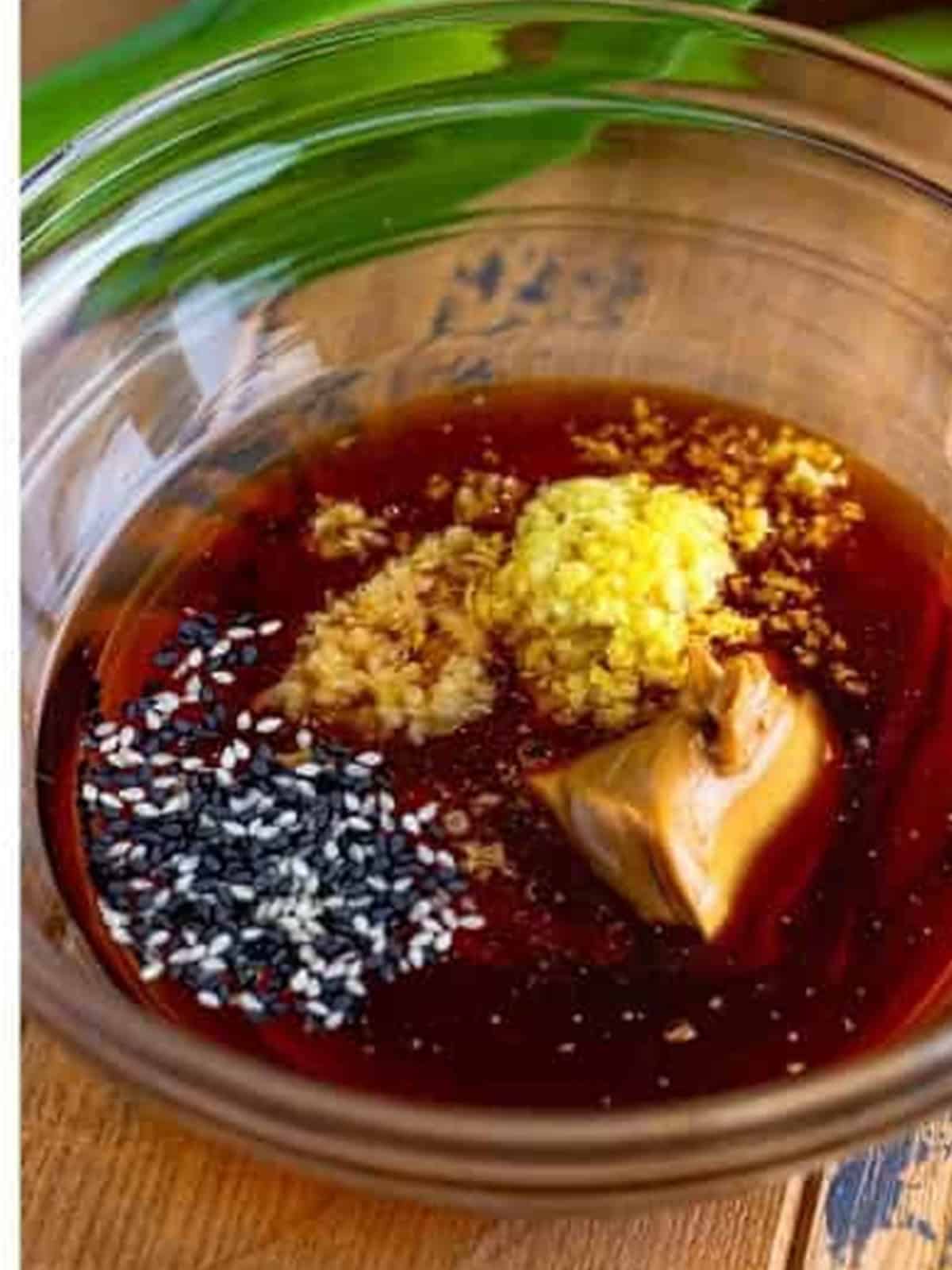 Dressing ingredients with ginger, garlic, and sesame in a glass bowl.